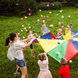 mom playing with a parachute and plastic balls with a bunch of children